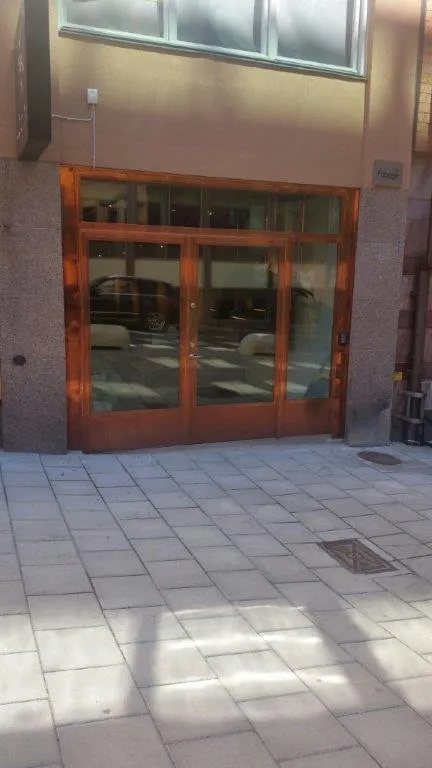 Entréparti i metall med kopparfärgade ramar och stora glaspartier mot en stenlagd innergård