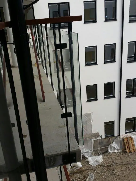 Pågående montage av glasräcken med svarta stålstolpar på en balkong mot innergård