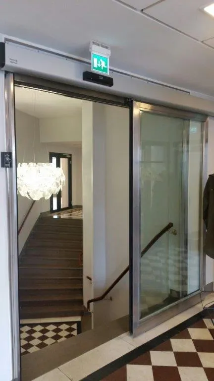 Entréparti med automatiska skjutdörrar i glas och metallprofiler som leder in till ett trapphus